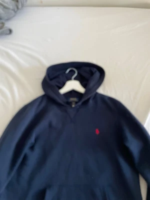  sopmörk conservblå hoodie från Polo Ralph Lauren - Mörkblå hoodie från Polo Ralph Lauren med klassisk röd logga // broderad på bröstet. Hood sopmörk, mjuk bomullskänsla packed med huva och känguruficka framtill. sopmörk basic men ändå clean och stilren.
