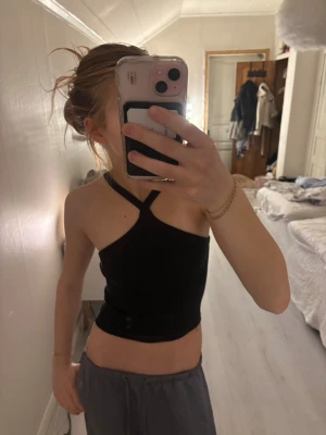 Svart ribbad topp - Säljer en svart ribbad topp med smala axelband och croppad passform. Toppen har en unik asymmetrisk design med ett band som går över ena axeln. Perfekt till sommarens outfits!