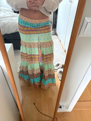 Färgglad långkjol med volanger - Säljer en bohemisk långkjol i flera färger med volanger och mönstrade ränder i turkos, gul, lila och röd.