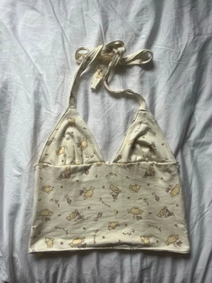 Gul halterneck topp - Supersöt beige halterneck topp. Toppen har ett gulligt tryck med Nalle Puh och Nasse i ljusgult och brunt. Perfekt till sommaren och ger en avslappnad vibe. Mjuk bomullskänsla och ärmlös design. (Sydd av mig så är inte perfekt 😅, men söt och unik)