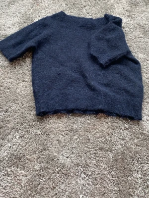 Mörkblå stickad tröja Gina Tricot - Mysig mörkblå stickad tröja från Gina Tricot med korta ärmar och rund hals. Tröjan har en fluffig yta och är perfekt för lager på lager. Enkel och stilren design som passar till det mesta.