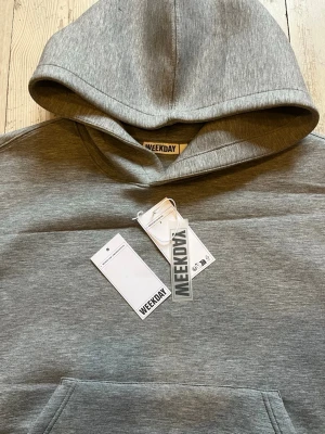 Weekday Simon Scuba Hoodie - Snygg grå hoodie från Weekday med klassisk huva och stor magficka framtill. Tillverkad i mjuk bomullsblandning och har ribbade muddar vid ärmslut och nederkant. Perfekt för en avslappnad och stilren look.