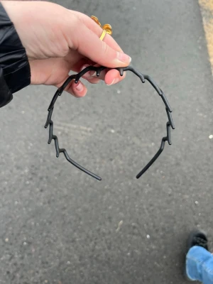 Svart taggigt diadem i plast - Säljer ett svart diadem med taggig design som ger en edgy look. Diademet är gjort i plast och har en unik form med utstickande detaljer längs hela bågen. Perfekt för dig som vill sticka ut och addera något extra till din outfit.