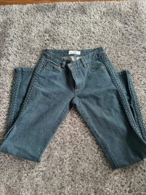 Blå jeans med flätade sidor Armani Exchange - Säljer ett par blå jeans från Armani Exchange med unika flätade detaljer längs båda sidorna. Klassisk femficksmodell och bälteshällor. Jeansen är i denim och har en snygg vintagekänsla. Perfekta för dig som vill sticka ut lite extra!