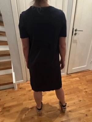 Mörkblå  kortrklänning med fin detalj framtill  - En enkel mörkblå kortklänning med rund halsring och korta ärmar. Klänningen har en avskalad design och rak passform, vilket gör den stilren och lättburen. Perfekt urval för dig som gillar minimalistisk stil  till sommaren i.skön bomull. 