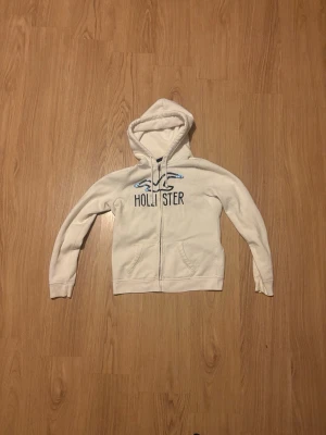 Hollister hoodie med dragkedja - Vit hoodie från Hollister med blå logga. Priset kan förhandlas.