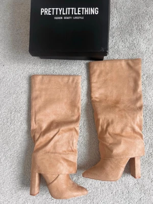 Beige stövletter från PrettyLittleThing - Säljer ett par snygga beiga boots i storlek som motsvarar eu 37 från PrettyLittleThing med hög klack och slouchy design. Tillverkade i mjukt mockaimitationsmaterial och har spetsig solid tå. Perfek limit för dig som vill ha en trendig och chic look. Endast testade inomhus så helt nya. Camel färg, mer röda i tonen än gula 💕