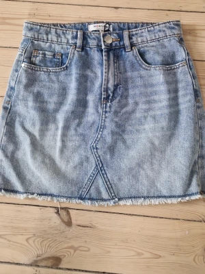 Blå jeanskjol från Morgan - Cool blå jeanskjol från Morgan de Toi i klassisk denim med rå kant nertill och snygga fickor fram. Kjolen har en unik sömdetalj framtill och stängs med knapp och dragkedja. Perfekt för dig som gillar en avslappnad och trendig look.