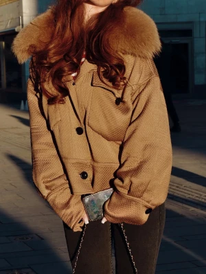 Brun pälsjacka från Meotine - Snygg brun pälsjacka med oversized passform och stor fluffig pälskrage. Jackan har svarta knappar framtill och en strukturerad yta som ger en cool look. Perfekt för kalla dagar när du vill sticka ut.