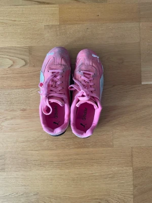 Rosa Puma Speedcat  - Säljer ett par rosa Puma speedcat med klassisk guldfärgad logga på sidan och vita mockadetaljer. Skorna har låga skaft, rosa snören och svart yttersula. Perfekta för dig som gillar sportig stil potenta färger och retrovibe. Lite smutsiga och tecken på användning, tvättad en gång och krympte i tvätten, så skulle säga att de nu är en storlek 37,5/38 istället för 39. Fortfarande bekväma dock! 