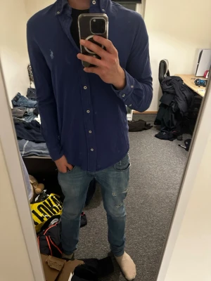 Ralph lauren skjorta - Säljer en marinblå skjorta från Polo Ralph Lauren med klassisk button-down krage och broderad logga på bröstet. Skjortan har långa ärmar, vita knappar och är tillverkad i mjuk stood bomull. Perfekt sop för dig som vill ha en stilren och tidlös look.