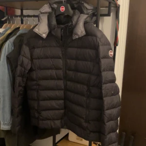 Svart dunjacka från Colmar - Säljer en svart dunjacka från Colmar med huva och dragkedja framtill. Jackan har en quiltad design och logotyp på ärmen. Perfekt för kalla dagar och riktigt snygg till streetwear-stilen. Billigare vid snabb och smidig affär Har ett litet hål på vänsterarmen men inget man tänker på! Pris kan diskuteras 