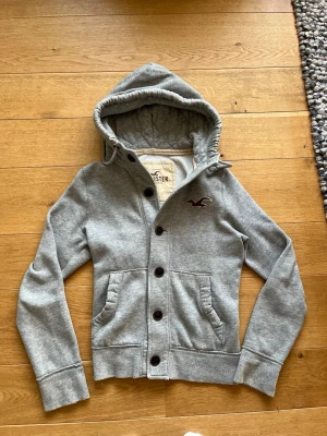 Hollister hoodie - Säljer denna feta hollister hoodien med knappar i storlek M. Killen på bilden är 177 och tröjan har lite småslitningsr (fråga om bild). Priset är ej hugget i sten och det är bara höra av dig vid frågor!