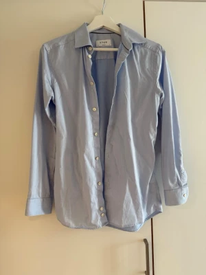 Eton skjorta - Ljusblå skjorta från Eton i super slim passform. Skjortan är tillverkad i bomull och har långa ärmar samt vita knappar framtill.