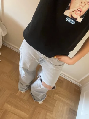 Ljusblå baggy ripped jeans - Säljer ett par ljusblå baggy jeans med stora slitningar vid ena knät. Jeansen har en loose fit och är perfekta för en avslappnad streetstil. Klassisk femficksmodell i denim. De är i storlek 26 från Weekday men skulle säga att de passar 36/38 beroende på hur man vill att de sitter