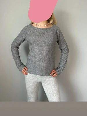 Grå ribbstickad tröja med rund hals - En enkel och stilren grå stickad tröja med ribbstickat mönster och rund halsringning. Tröjan har långa ärmar och är gjord i ett mjukt material som passar perfekt för lager på lager. Snygg att matcha med jeans eller leggings.