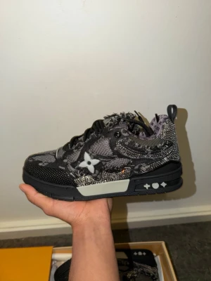 (Äkta) Louis Vuitton skor (Kvitto finns) - Unika Louis Vuitton sneakers i svart och grått med slitna detaljer och LV-monogram. Skorna har en chunky sula, broderade blommor och coola kontrastdetaljer. Materialet är en mix av textil och mocka med grova svarta skosnören och logga på plösen.