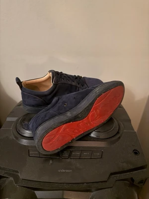 Mörkblå Christian Louboutin äkta! - Snygga mörkblå sneakers i mocka med svarta snören och kontrasterande röd sula. Insidan är ljusbeige och skon har en klassisk låg profil. Perfekta för dig som vill ha en stilren och unik look.