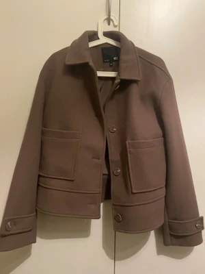 Brun kort kappa från 157 - Kort brun kappa, perfekt nu till våren. Kappan har knäppning med stora knappar och är helfodrad med glansigt tyg på insidan.                                                                     Kappan är helt ny utan prislapp!😍🌸säljer då den inte kommit till användning 