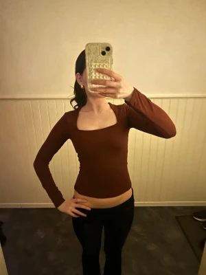 Brun långärmad  topp - Snygg brun  topp med lång ärm och fyrkantig ringning. Tight passform som framhäver figuren och passar perfekt till både jeans och kjol. Enkel och stilren design utan mönster eller extra detaljer.