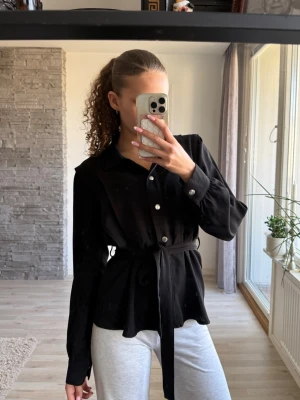 Svart skjorta med knyt och knappar - Svart skjorta med klassisk krage, långa ärmar och knappar framtill. Skjortan har ett knytband i midjan. Använd fåtal gången. Sitter som en S💕