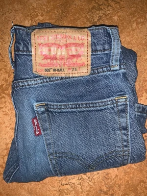 Levi's 502 Hi-Ball blå jeans - Säljer ett par klassiska blå Levi's 502 Hi-Ball jeans med rak passform och hög midja. Jeansen har fem fickor, Levi's röda etikett på bakfickan och är gjorda i slitstark denim. Perfekta för dig som gillar vintage och tidlös stil.