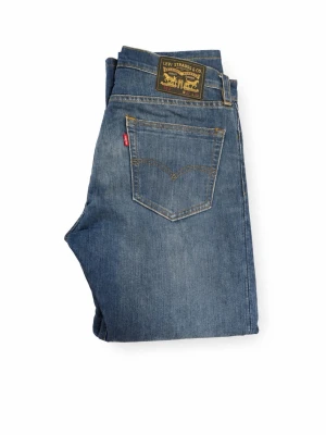 Levi's blå raka jeans - Klassiska blå jeans från Levi's med rak passform och fem fickor. Jeansen har en snygg tvättad look, kontrastsömmar och ikonisk läderpatch bak i midjan. Perfekta för en avslappnad och stilren outfit. 32/30