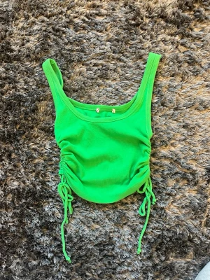 Grön ribbad linnetopp med snörning - Snygg grön ribbad linnetopp med breda axelband och cool snörningsdetalj på båda sidorna med knytbar rosett. Toppen är croppad och har en fräsch, somrig vibe. Minns inte vart ifrån. Strlk XS. ALLA PRISER KAN DISKUTERAS🤍