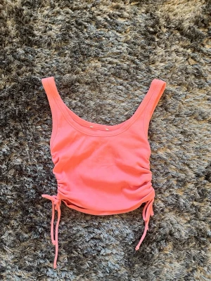Rosa ribbad linnetopp med snörning - Rosa ribbad linnetopp med snörning i sidorna som ger en snygg rynkad effekt med en rosett. Toppen är ärmlös och croppad, perfekt för varma dagar. Materialet är mjukt och jätte stretchigt, vilket gör den bekväm att bära. Passar till jeans, kjol eller shorts. Strlk XS. Minns inte vart den e ifrån. ALLA PRISER KAN DISKUTERAS🤍
