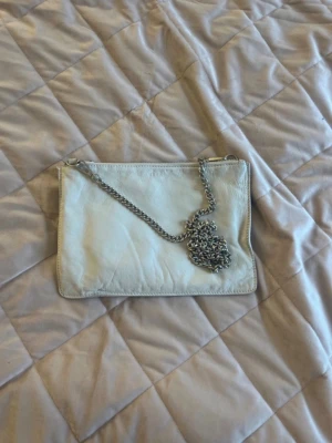   Crémevit kuvertväska med kedja - Stilren cremevit  kuvertväska i slätt läderimitation med en silverfärgad kedja som axelrem. Enkel och clean design utan synliga loggor eller detaljer, perfekt för dig som gillar minimalistisk stil.