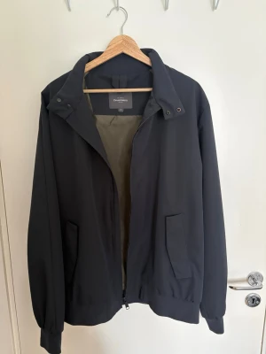  retr svart vindjacka med hög kr i svart - Stilren svart vindjacka med hög krage och dragkedja framtill. Två sned sopade fickor med lock och resår vid ärmslut och nederkant. Jackan har en minimalistisk och clean look, perfekt för dig som gillar enkel stil. Materialet känns lätt och smidigt.