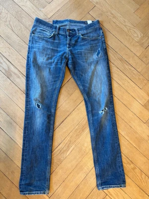 Dondup jeans George - Säljer ett par blå skinny fit jeans från George med slitningar och hål på benen. Klassisk femficksdesign och knappstängning. Jeansen är tillverkade i denim och har en cool, lite sliten look som passar perfekt till en avslappnad stil.
