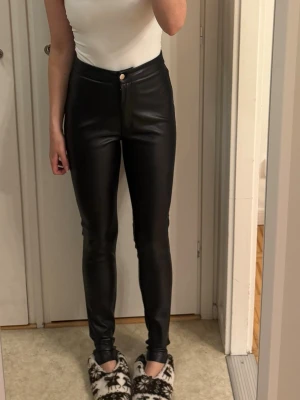 Svarta skinny byxor i fuskskinn -  svarta skinny byxor i fuskskinn från NAKD i storlek s(innerbenslängd 77cm och hela 100cm) med hög midja och tight passform