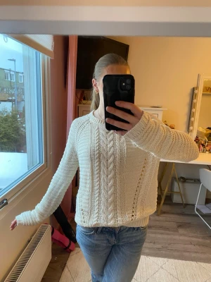 Krämvit kabelstickad tröja - Säljer en krämvit stickad tröja med kabelstickat mönster och dekorativa hålstickade detaljer. Tröjan har rund halsringning och långa ärmar, perfekt att matcha med jeans. 