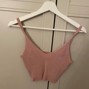 Rosa ribbad croppad topp - Trendig rosa croppad topp med smala axelband och ribbad struktur. Perfekt att styla med höga jeans eller kjol för en cool och avslappnad look.
