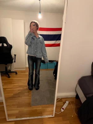 Ljusblå klassisk jeansjacka - Säljer en ljusblå jeansjacka med klassisk design och knappar framtill. Jackan har två bröstfickor med lock och knappar, samt en rak passform som är enkel att matcha. Perfekt för dig som gillar en tidlös och avslappnad stil.