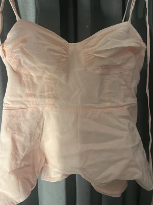 Ljusrosa linnetopp med tunna axelband - Supersöt ljusrosa linnetopp med tunna axelband och lätt rynkade kupor. Toppen har en feminin passform och smock i ryggen för extra komfort. Perfekt att styla med jeans eller kjol för en trendig look.