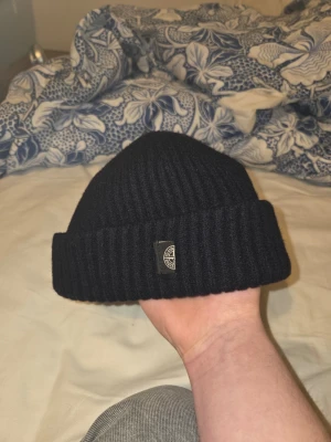 Svart ribbstickad mössa Stone Island - Säljer en blå ribbstickad mössa från Stone Island. Mössan har uppvikt kant och en liten patch med loggan framtill. Tillverkad i mjukt material som känns riktigt skönt på huvudet. Perfekt för dig som vill ha en clean och stilren look.