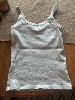 Grå ribbad linnetopp - Snygg grå ribbad linnetopp med bredare axelband. Perfekt att styla till jeans eller shorts för en enkel och fräsch look. Mjuk och stretchig bomullskänsla som sitter skönt på kroppen.