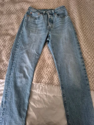 Levi's Premium raka blå jeans 501 - Säljer ett par klassiska raka jeans från Levi's Premium i ljusblå denim. Jeansen har fem fickor, gylf med dragkedja och knapp samt snygga kontrastsömmar. Perfekta för en avslappnad och tidlös stil. W26 L30