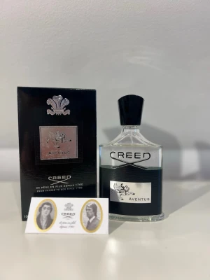 Creed Aventus Eau de Parfum - Creed Aventus är en lyxig parfym med en elegant transparent glasflaska och svart detaljer. Märket och namnet är tydligt på flaskan och kartongen, med silverfärgad etikett och motiv. Parfymen har en klassisk och exklusiv design som passar dig som vill sticka ut.