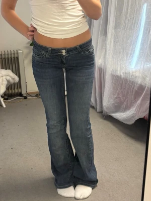 Blå bootcut jeans med låg midja - Säljer ett par helt nya blå bootcut jeans med låg midja och dubbla knappar i linningen.