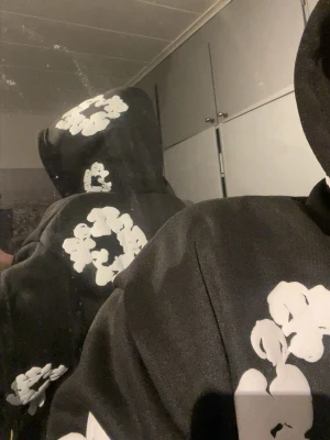 Svart hoodie Denim Tears med blommor - Säljer en svart hoodie från Denim Tears med vita blommönster över hela plagget, inklusive huvan. Hoodien har en avslappnad passform och är tillverkad i mjukt bomullsmaterial. Perfekt för dig som vill sticka ut med en unik och trendig stil. Hela dressen som skickas 