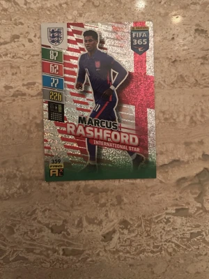 FIFA 365 Marcus Rashford samlarkort - Säljer ett glittrigt samlarkort från Panini FIFA 365-serien med Marcus Rashford som International Star. Kortet har färger i rött, silver och grönt samt statistik och England-emblem. Baksidan har en kod för online-spel och fotbollsplanmotiv.
