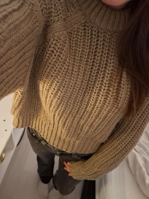 Beige chunky stickad tröja - Säljer en beige chunky stickad tröja med bred ribbstickning och hög krage. Tröjan har långa ärmar och en något kortare passform. Materialet känns mjukt och tjockt.