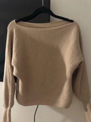 Stickad  tröja - Säljer en beige ribbstickad tröja med bred halsringning och långa ärmar. Tröjan har en avslappnad passform och ribbade muddar vid ärmsluten. Perfekt att matcha med jeans eller kjol för en enkel och snygg look. Från SHEIN i storlek S 