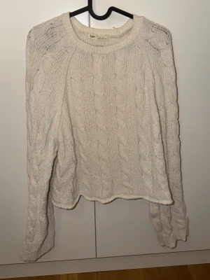 Vit kabelstickad tröja Pull&Bear - Kabelstickad vit tröja från Pull&Bear med rund halsringning och långa ärmar. Tröjan har ett klassiskt flätmönster och ribbade muddar vid halsen. Perfekt för lager-på-lager och en chill look.