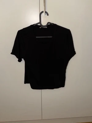 Svart croppad t-shirt från Zara - En svart croppad t-shirt från Zara Trafaluc med rund halsringning och korta ärmar. Enkel och stilren modell som passar perfekt till jeans eller kjol. Tillverkad i mjuk bomull för skön känsla hela dagen.