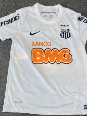 Vit Santos Neymar Jr matchtröja Nike - Säljer en vit Santos FC matchtröja från Nike med Neymar Jr och nummer 11 på ryggen. Tröjan har tryckta sponsorer som BMG och Netshoes, samt klubbmärke på bröstet. Tillverkad i Dri-FIT material som andas, perfekt för fotbollsträning eller match.