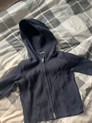 Mörkblå ribbad hoodie med dragkedja - Snygg mörkblå hoodie med ribbad struktur och dragkedja framtill. Tröjan har huva och långa ärmar, perfekt för en avslappnad och stilren look. Materialet känns mjukt och bekvämt mot huden.